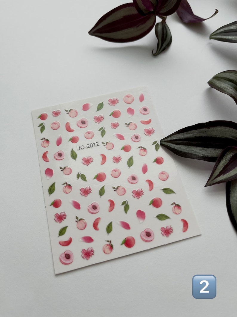 May include: A sheet of peach-themed nail stickers with pink peaches, green leaves, and pink flower petals. The sheet is labeled "JO-2012".