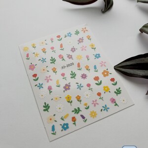May include: A sheet of colorful flower stickers with a white background. The stickers feature various flowers in shades of pink, yellow, blue, and green. The sheet is labeled "JO-2020" in the center.