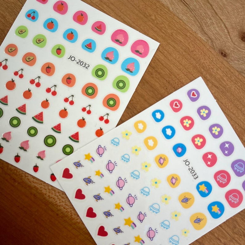 May include: Two sheets of colorful stickers with various designs. The first sheet features fruit and food designs, including watermelon, kiwi, cherries, and peaches. The second sheet features space-themed designs, including planets, stars, rockets, and clouds. The text "JO-2032" and "JO-2033" is printed on each sheet.