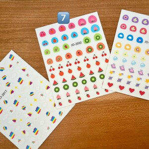 May include: Four sheets of colorful stickers with different designs. The first sheet has rainbow-colored shapes, the second sheet has fruit designs, the third sheet has fruit designs, and the fourth sheet has space-themed designs. The sheets are labeled with the numbers 6, 7, and 8.