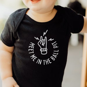 May include: A black baby onesie with a white graphic of a hand making a rock and roll sign with the text "Meet me in the ball pit".