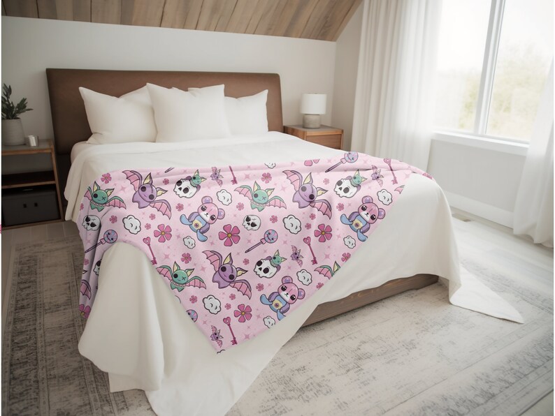 K&ouml;nnte beinhalten: Eine rosa Fleece-Decke mit einem sich wiederholenden Muster aus niedlichen Cartoon-Flederm&auml;usen, Sch&auml;deln, Blumen und Wolken. Die Flederm&auml;use sind lila und gr&uuml;n mit rosa Fl&uuml;geln. Die Sch&auml;del sind wei&szlig; mit rosa Akzenten. Die Blumen sind rosa und wei&szlig;. Die Wolken sind wei&szlig;.