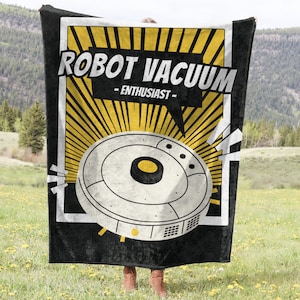 May include: Black blanket with a retro-style graphic featuring a robot vacuum cleaner design. The text "ROBOT VACUUM - ENTHUSIAST" is displayed in a bold font. The design includes yellow sunburst rays and a white border.