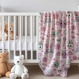 K&ouml;nnte beinhalten: Eine rosa Babydecke mit einem niedlichen Cartoon-Muster mit Flederm&auml;usen, Sch&auml;deln, Herzen und Blumen. Die Decke ist weich und kuschelig, perfekt f&uuml;r ein Babyzimmer.