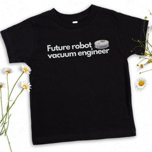 May include: Black t-shirt with white text that reads "Future robot vacuum engineer." A graphic of a robot vacuum cleaner is above the text. The shirt is surrounded by white daisies with yellow centers.