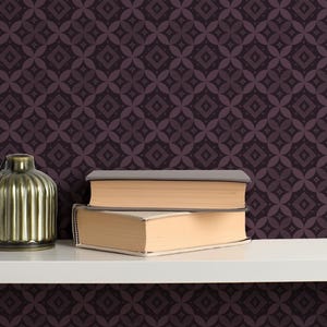 May include: A decorative still life featuring a green ribbed vase and two books with beige pages and gray covers. The items are arranged on a white shelf against a patterned dark purple background.