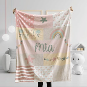 May include: A pink and beige patchwork baby blanket with a rainbow, stars, and the text "Sweet Dreams" and "mia".