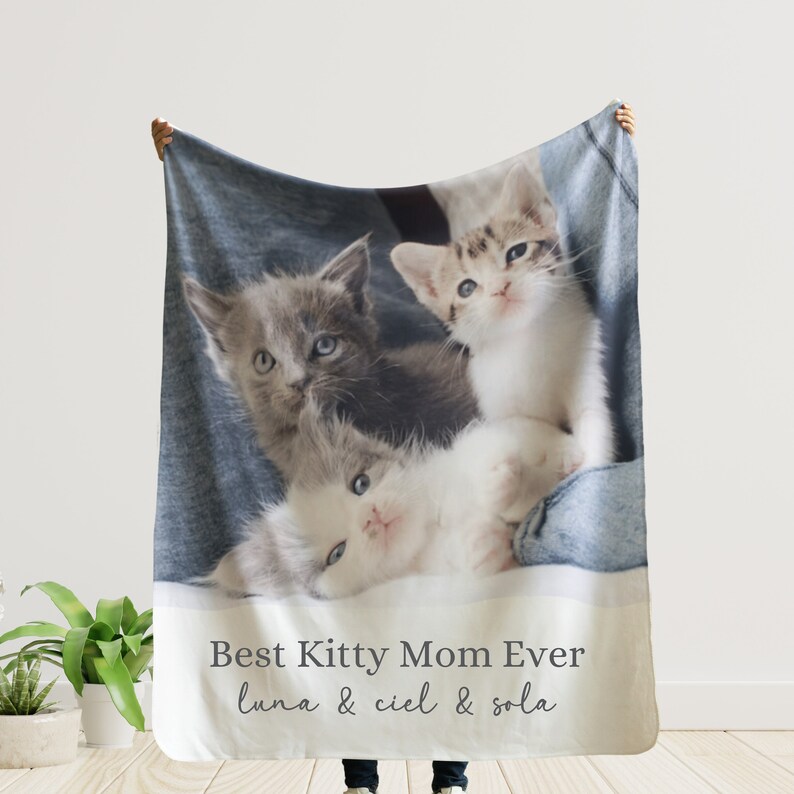 May include: A blue fleece blanket with a photo of three kittens cuddling. The text "Best Kitty Mom Ever luna & ciel & sola" is printed on the bottom of the blanket.