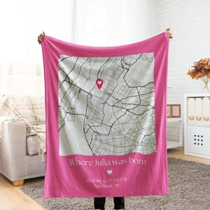 May include: Pink fleece blanket with a map of New York City and a red heart marking a location. The text "Where Julia was born" and the coordinates "40.7646 N, 73.9743 W" are printed below the map.  New York, NY is printed below the coordinates.