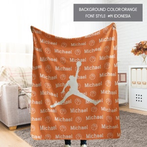 May include: An orange fleece blanket with a white basketball silhouette and the name "Michael" repeated throughout. The text is in a bold, blocky font.