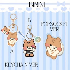 May include: Image features three items: two keychains and a PopSocket. The keychains have a gold-colored clasp and a cartoon bear design. The PopSocket also has the bear design. Text on the image includes "BININI", "KEYCHAIN VER", and "POPSOCKET VER".