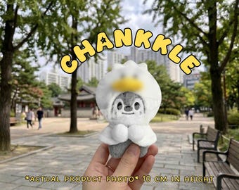 May include: A small gray plush toy wearing a white hood with a yellow accent, featuring the text CHANKKLE at the top and the text ACTUAL PRODUCT PHOTO 10 CM IN HEIGHT at the bottom. The plush has a rounded shape with small white paws.