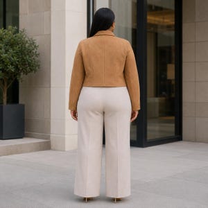 May include: A tan suede jacket with a collared neckline and long sleeves. The jacket is paired with cream-colored wide-leg pants. The outfit is suitable for a professional or casual setting.