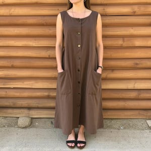 May include: A brown sleeveless maxi dress with a button-up front and two large pockets. The dress is made of a linen-like fabric.
