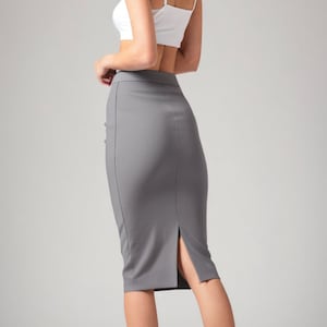 May include: A woman wearing a white crop top and a gray pencil skirt with a slit in the back. She is wearing black heels.