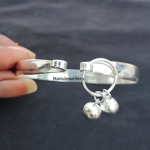 May include: Silver baby bangle with two dangling bells. The bangle is open and has a smooth, polished finish.