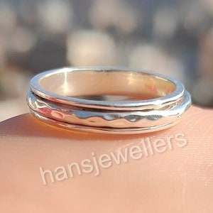 Może przedstawiać: Srebrny pierścień obrotowy z fakturą młotkową. Pierścień ma trzy paski, które obracają się niezależnie.