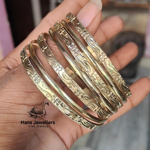 Puede incluir: Un conjunto de siete brazaletes de color dorado con diseños florales. Los brazaletes están apilados uno encima del otro y se llevan en la muñeca.