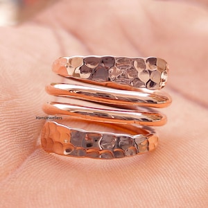 Könnte beinhalten: Ein roségoldener Hammerring mit vier Bändern. Das obere Band ist gehämmert, die anderen drei Bänder sind glatt.