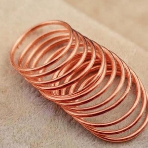 May include: A stack of multiple thin, circular copper-coloured metal rings. Each ring features a smooth, polished surface with a consistent round shape, arranged in a slightly overlapping, angled formation to display the metallic texture.