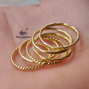 May include: A set of five gold-toned stacking rings. The rings are different widths and have a variety of textures, including smooth, hammered, and twisted.