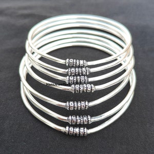 May include: A set of six silver bangles with a textured design. The bangles are stacked on top of each other and have a shiny finish.