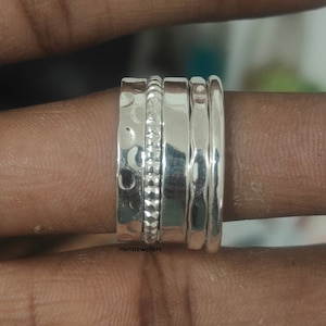 Könnte beinhalten: Ein Satz von vier silbernen Stapelringen. Die Ringe sind alle unterschiedlich breit und haben unterschiedliche Texturen. Die Ringe werden an einem Finger getragen.