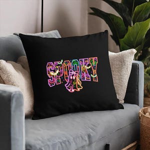 May include: Black throw pillow with the word "SPOOKY" in colorful, Halloween-themed lettering. A ghost illustration is below the word. The pillow is on a gray couch with white and beige pillows.