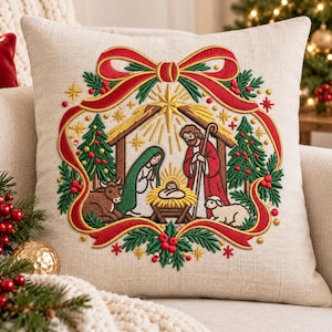 May include: A square beige throw pillow featuring a central embroidered nativity scene. The design includes a stable, a star, figures of Mary, Joseph, and the infant Jesus, a cow, and a sheep, all framed by a red ribbon and green holly.