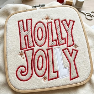Op de afbeelding: Een vierkant houten borduurraam met een witte, textuurrijke stof waarop de tekst HOLLY JOLLY is geborduurd. De letters hebben een rode omlijning en een beige stippenpatroon, behalve de laatste letter L die effen wit is. Gouden sterren omringen de tekst.