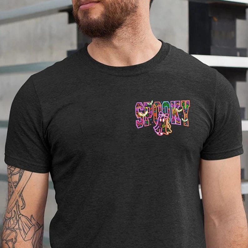 May include: Dark gray t-shirt with the word "SPOOKY" in colorful, neon-style lettering. A small ghost graphic is below the word. The shirt is a crew neck style.