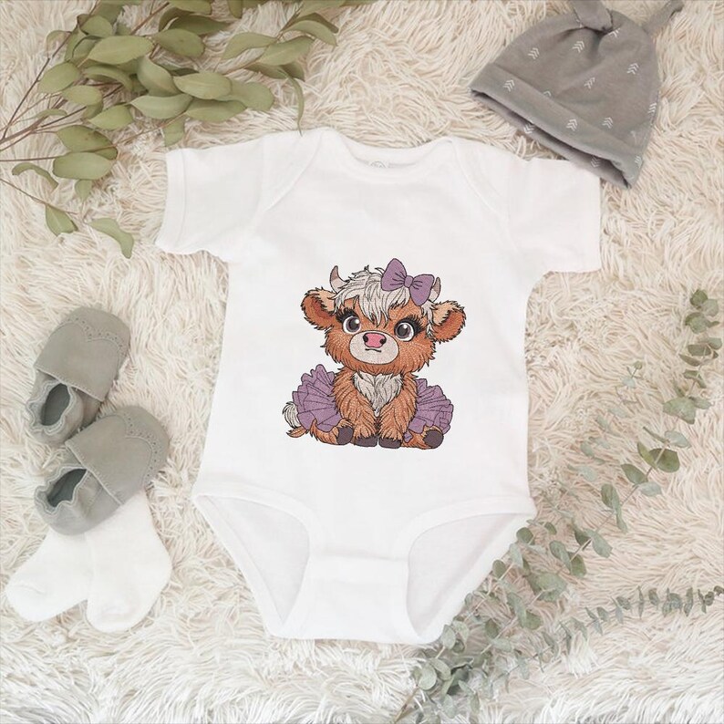 May include: White baby onesie with a brown and white cow wearing a purple tutu and a purple bow. The cow is looking to the left.