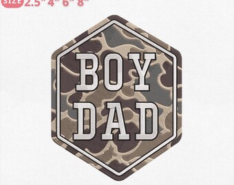 May include: A camouflage-patterned patch with the words "BOY DAD" in white block letters. The patch is in a hexagonal shape and includes text indicating embroidery file sizes of 2.5", 4", 6", and 8".