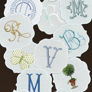 May include: A collection of white, scalloped-edge coasters with embroidered designs. The designs include various letters, a butterfly, and a small tree. The embroidery features colors like blue, green, gold, and pink.