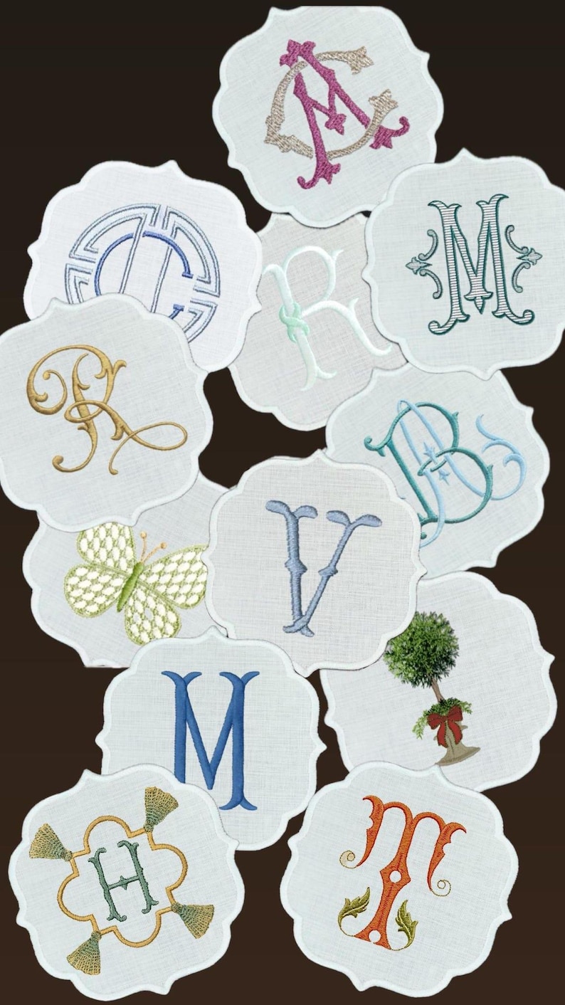 May include: A collection of white, scalloped-edge coasters with embroidered designs. The designs include various letters, a butterfly, and a small tree. The embroidery features colors like blue, green, gold, and pink.