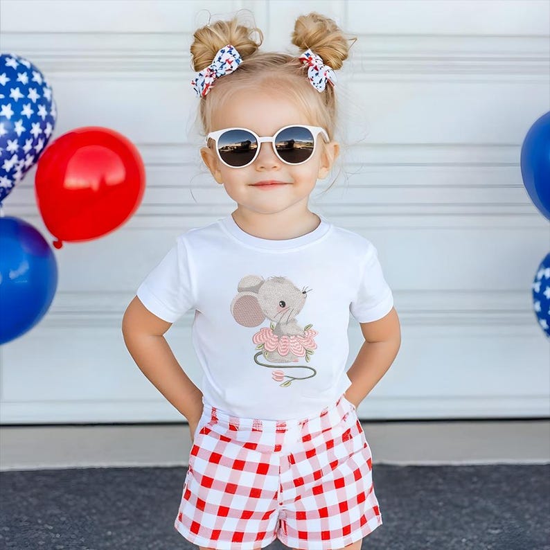 May include: A child wearing round white sunglasses, a white t-shirt with a mouse graphic, and red and white gingham shorts. The child has two hair buns with red, white, and blue bow hair clips. Balloons in red, blue, and white are in the background.