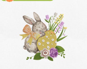 May include: Machine embroidery design of a gray bunny holding a yellow Easter egg with white polka dots. The bunny has a yellow bow and is surrounded by green leaves and purple flowers.