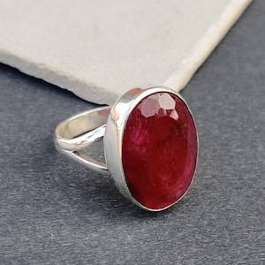 May include: A silver ring with a large, oval-shaped, red gemstone. The ring has a simple, elegant design.