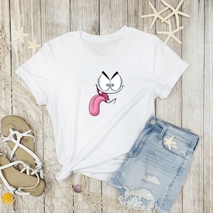 Puede incluir: Camiseta blanca con un gr&aacute;fico de cara de dibujos animados. La cara est&aacute; haciendo una expresi&oacute;n divertida con la lengua fuera y una gota de sudor goteando.