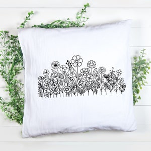 May include: A white pillow with a black line drawing of a field of flowers. The flowers are stylized and have simple shapes.