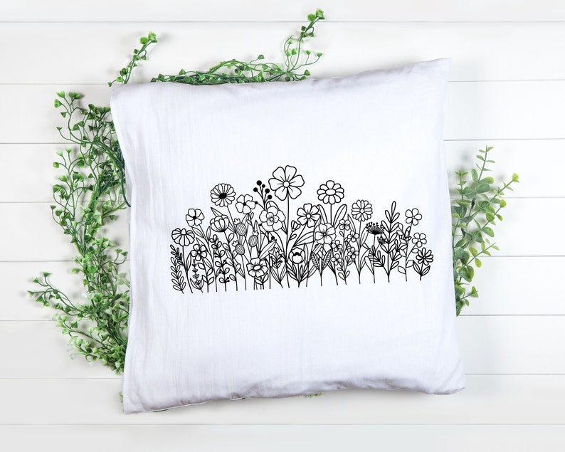 May include: A white pillow with a black line drawing of a field of flowers. The flowers are stylized and have simple shapes.