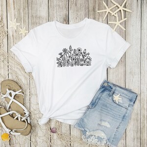 May include: White t-shirt with a black line drawing of a cluster of flowers on the front.