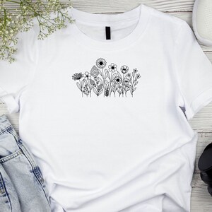 May include: White t-shirt with a black line drawing of a cluster of flowers on the front.