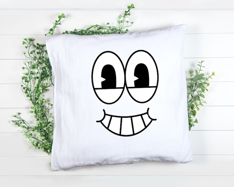 Puede incluir: Funda de almohada blanca con una cara de dibujos animados en blanco y negro impresa en ella. La cara tiene dos ojos grandes, una amplia sonrisa y dientes.