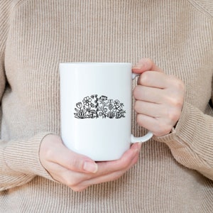 May include: White ceramic mug with a black line drawing of a cluster of flowers and leaves.