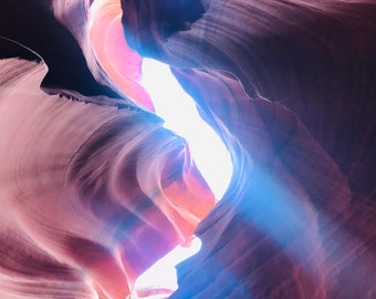 May include: A narrow canyon with smooth, swirling, red rock walls. A beam of light shines through a gap in the rock, illuminating the canyon.