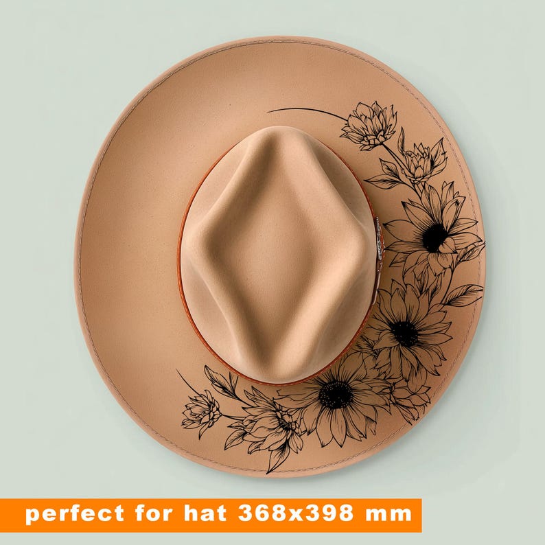 May include: A tan-coloured hat with a wide brim and a decorative floral design. The hat features a brown band and a crown. The brim is adorned with a black floral pattern. The hat measures 368 x 398 mm.
