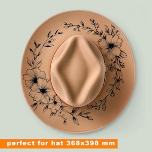 May include: A tan-coloured fedora-style hat with a floral design. The hat features a light brown crown and brim, with a black floral pattern around the brim. The hat measures 36.8 x 39.8 cm.