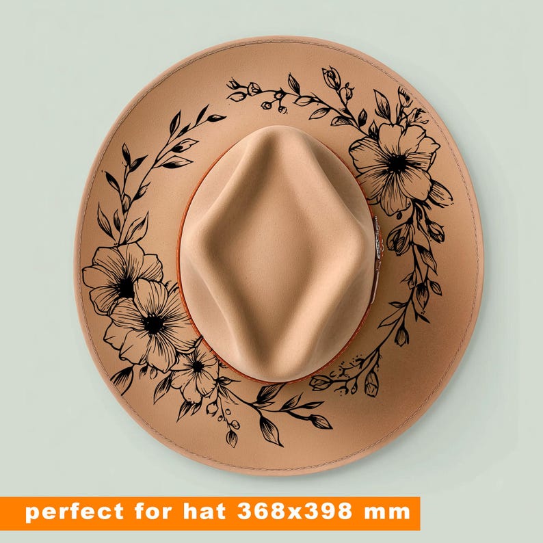 May include: A tan-coloured fedora-style hat with a floral design. The hat features a light brown crown and brim, with a black floral pattern around the brim. The hat measures 36.8 x 39.8 cm.
