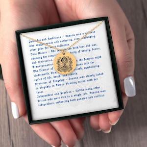 May include: A gold-colored pendant necklace with a round charm featuring a detailed design. The necklace is presented in a black box with text on a white background. The text describes Inanna's characteristics.